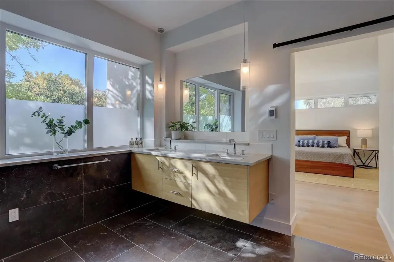 Floating wood vanity with stone countertop and a pocket door to the bedroom