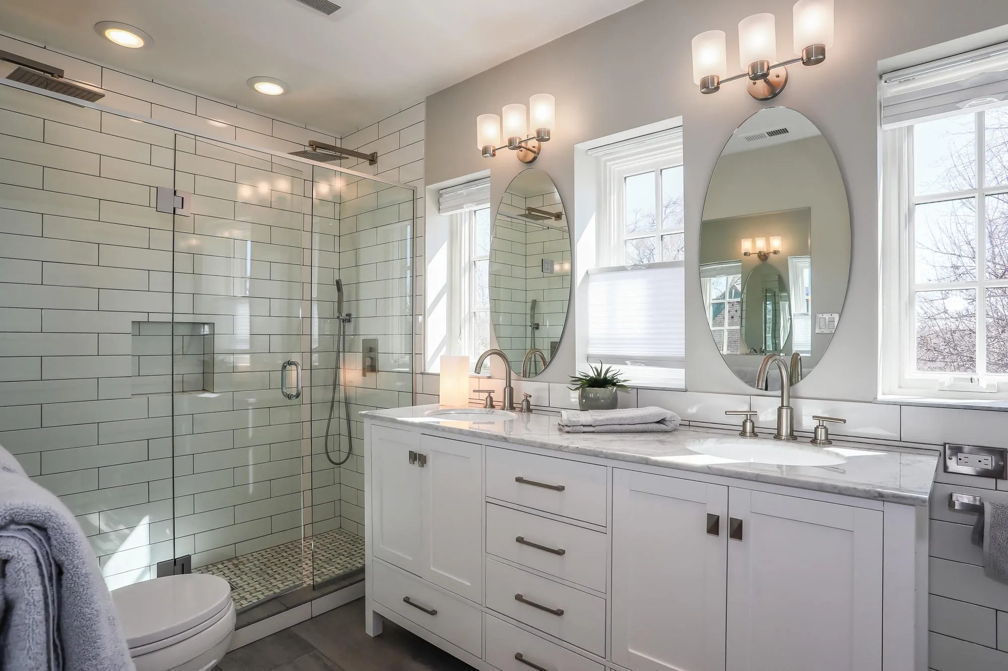 White Shaker double vanity with oval mirrors and a glass shower